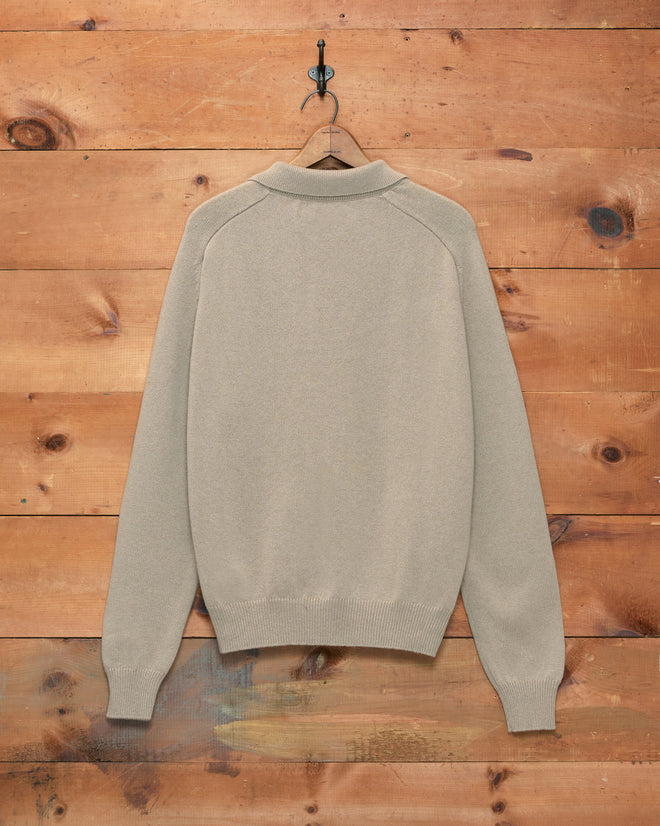 An Oatmeal Cashmere Polo from the 1960s hangs on a wooden wall, displayed from the back on a single hook.