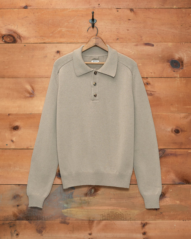 Oatmeal Cashmere Polo with long sleeves and a classic collared button design, inspired by timeless 1960s sweater styles, displayed against a wooden wall.