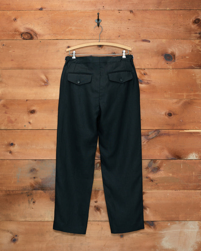 Lightweight Linen Side-Buckle Trousers in black, displayed from the back on a wooden hanger against a rustic wooden wall.