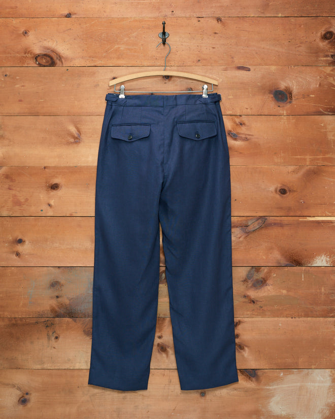 Lightweight Linen Side-Buckle Trousers in Midnight, designed for men, displayed on a wooden hanger against a rustic wooden wall backdrop.