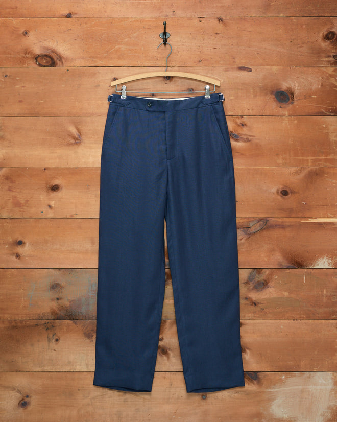The Lightweight Linen Side-Buckle Trousers - Midnight hang on a wooden hanger against a rustic wooden wall background, offering the perfect choice for men’s summer trousers.