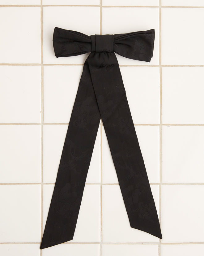 A large Football Jacquard Bow Barrette in black, featuring long tails and crafted from vintage-inspired deadstock woven fabric, is displayed on a white tiled surface.