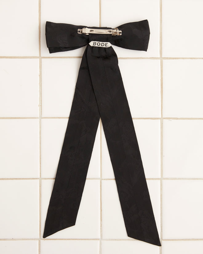 A large Football Jacquard Bow Barrette in black, featuring long tails and crafted from vintage-inspired deadstock woven fabric, is displayed on a white tiled surface.