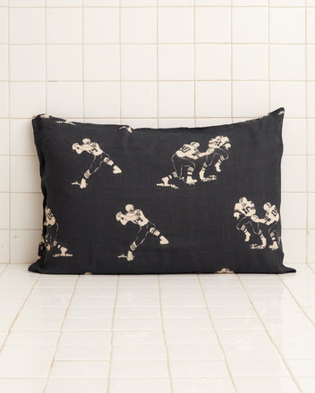 The Football Silhouette Pillowcases - Black/Cream feature white, hand-embroidered illustrations of football players in various action poses against a black, tiled backdrop.