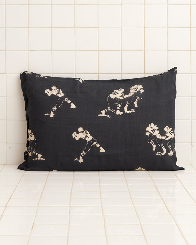 The Football Silhouette Pillowcases - Black/Cream feature white, hand-embroidered illustrations of football players in various action poses against a black, tiled backdrop.