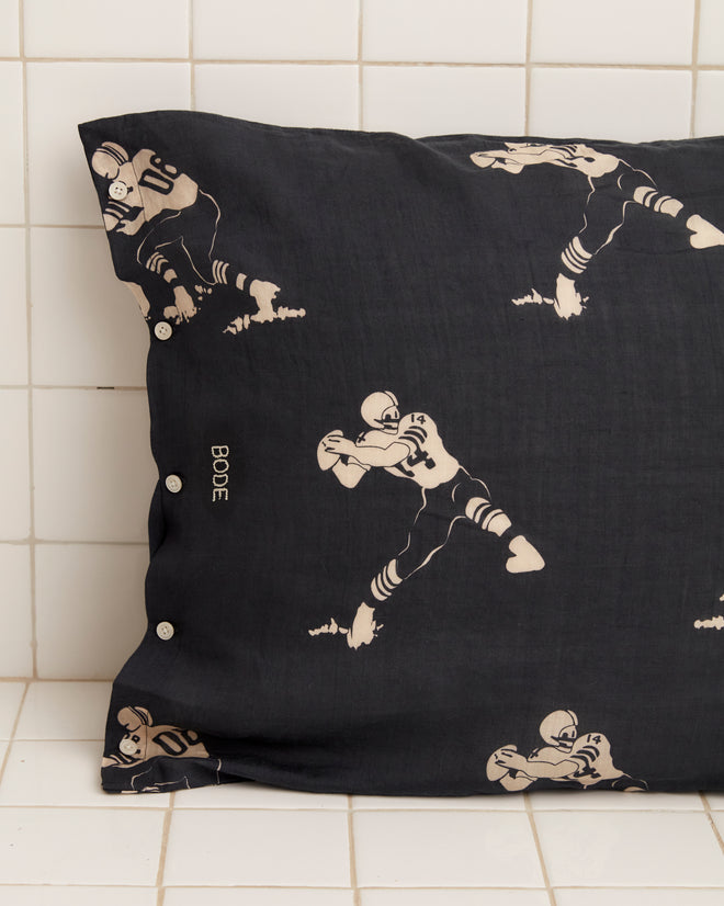 The Football Silhouette Pillowcases - Black/Cream feature white, hand-embroidered illustrations of football players in various action poses against a black, tiled backdrop.