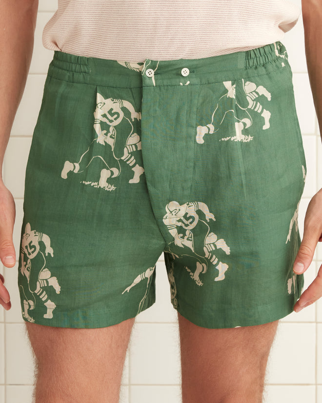 Green linen boxer shorts images of football players across the garment. Features elastic side bands and a two button front closure.