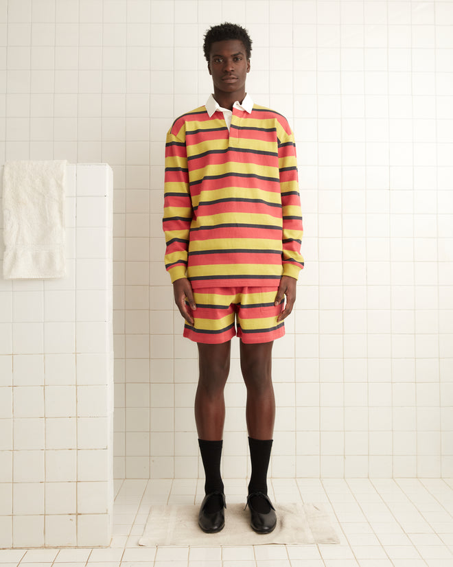 A person wearing Rec Stripe Sweatshorts, designed with a colorful 1980s style, stands in a tiled room with a towel hanging on the wall.