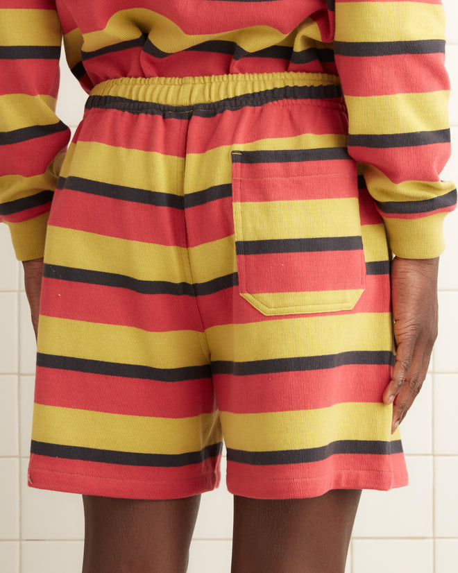 A person wearing Rec Stripe Sweatshorts, designed with a colorful 1980s style, stands in a tiled room with a towel hanging on the wall.