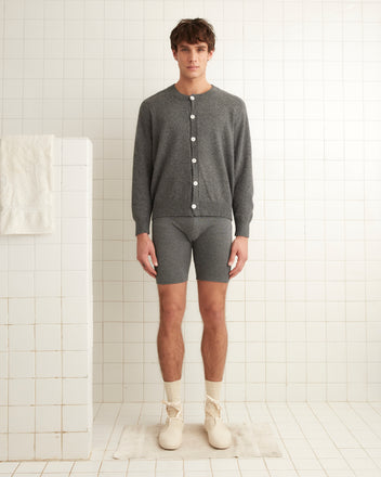 A person stands in a tiled room wearing a gray cardigan made of Royal Alpaca, Lounge Shorts - Grey, cream socks, and shoes.