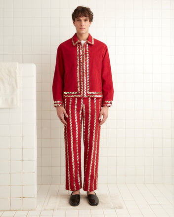 A person wearing a Bandstand Jacket in red, featuring gold sequin trim, stands in a tiled room next to a white towel on a rack.