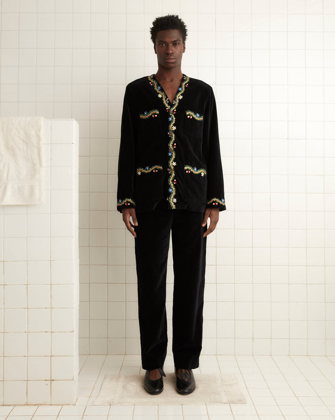 Person in an Alpineflower Jacket, featuring vintage-inspired floral embroidery, stands in a tiled room with a towel on the towel rack.