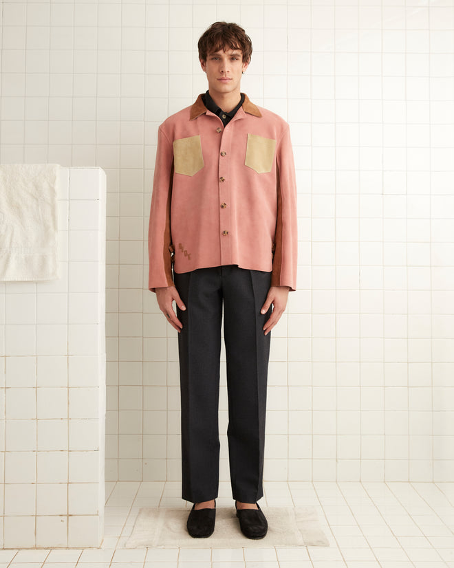 A person wearing a Buckled Multi-Suede Work Shirt in pink and dark pants stands in a room with white tiles.