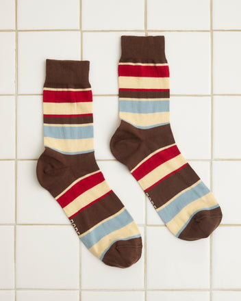 The Tournament Socks - Maroon/Multi, a vintage pair featuring multicolored stripes in brown, red, blue, and beige bands, lie flat on a white tiled surface.