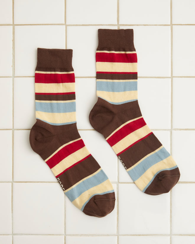 The Tournament Socks - Maroon/Multi, a vintage pair featuring multicolored stripes in brown, red, blue, and beige bands, lie flat on a white tiled surface.