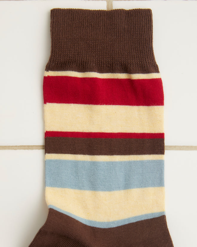 The Tournament Socks - Maroon/Multi, a vintage pair featuring multicolored stripes in brown, red, blue, and beige bands, lie flat on a white tiled surface.