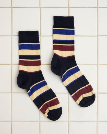 A pair of Tournament Socks - Navy/Multi showcasing a vintage stripe pattern with horizontal stripes in black, beige, burgundy, and blue laid out on a white tiled surface.