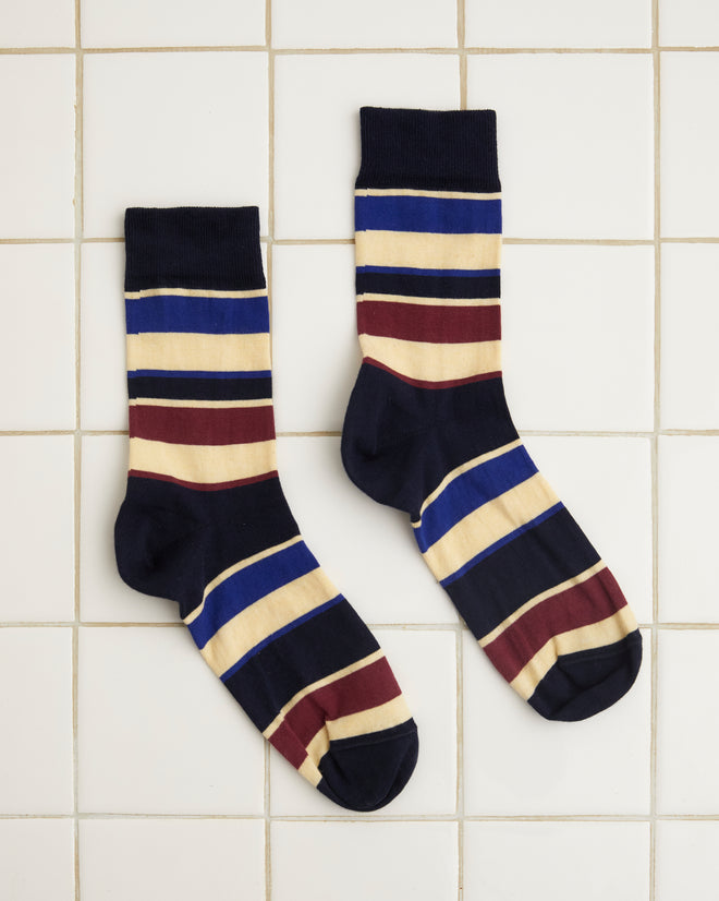 A pair of Tournament Socks - Navy/Multi showcasing a vintage stripe pattern with horizontal stripes in black, beige, burgundy, and blue laid out on a white tiled surface.