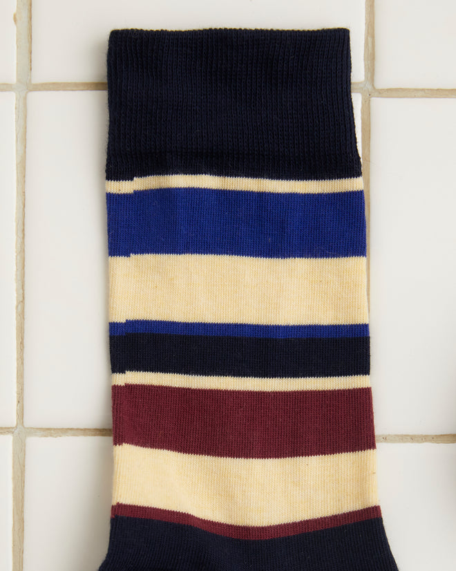 A pair of Tournament Socks - Navy/Multi showcasing a vintage stripe pattern with horizontal stripes in black, beige, burgundy, and blue laid out on a white tiled surface.