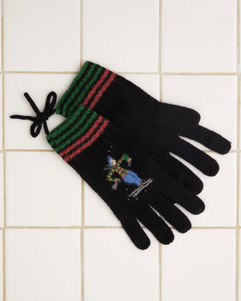 The Ski Run Gloves, made of soft merino wool, feature green and red stripes along with hand-embroidered skier motifs, elegantly displayed on a tiled surface.