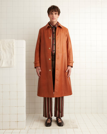 A person stands in a tiled room, draped in a Continental Coat with a throat latch collar over a patterned outfit and shoes.