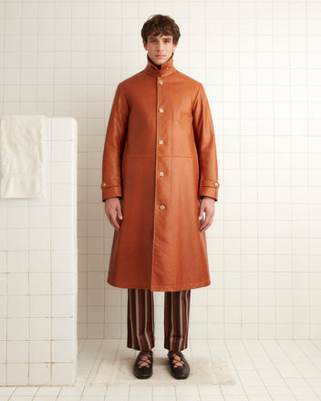 A person stands in a tiled room, draped in a Continental Coat with a throat latch collar over a patterned outfit and shoes.