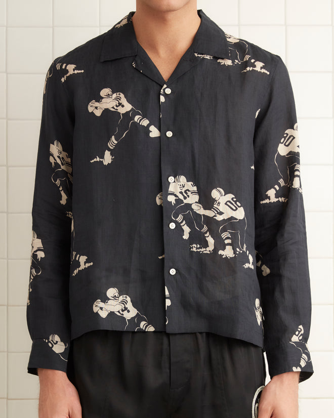 Black linen long sleeve shirt with images of football players across the garment. Five button down front seam with pointed collar.