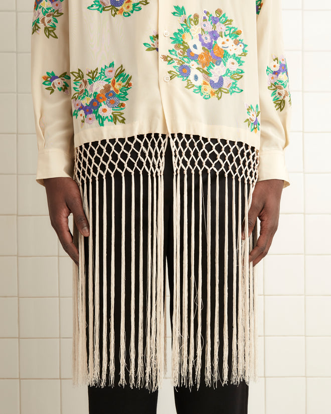 A person wearing the Flower Language Shirt with fringe stands in a tiled room, paired with black pants and shoes, beside a towel.