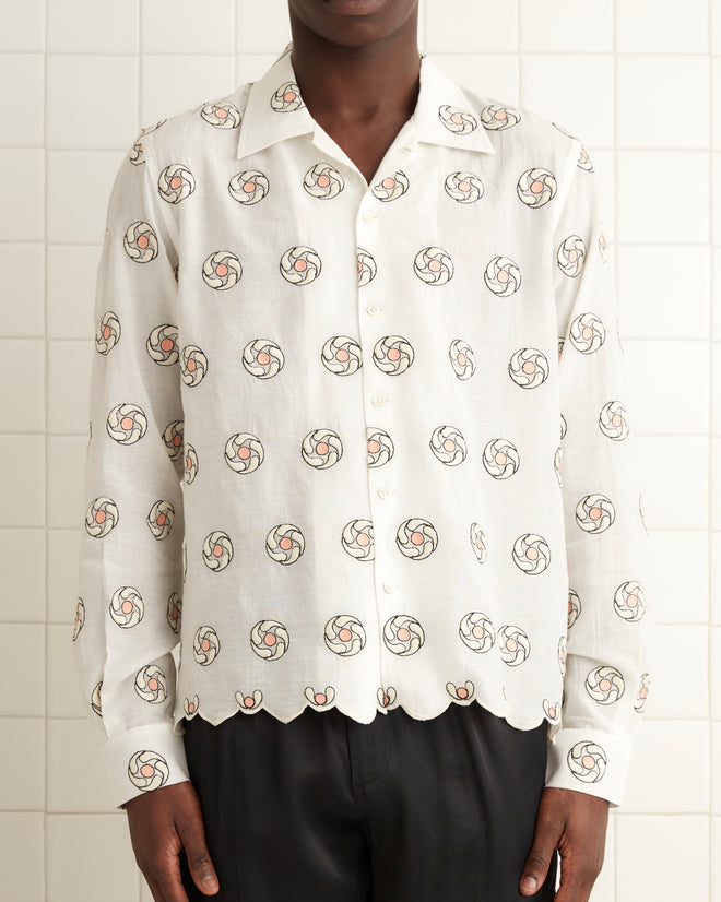 A person stands in a tiled room, wearing the Floral Aperture Long Sleeve Shirt paired with black pants. A towel hangs on the tiled wall, enhancing the room's simple elegance.