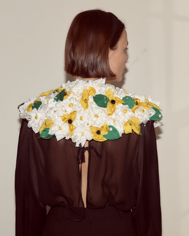Woman with brown bob haircut, wearing a sheer black top and the Blossom Collar, which is adorned with white and yellow fabric flowers.