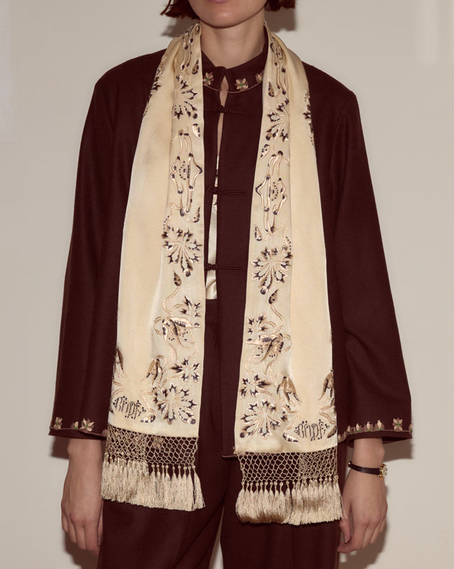 Person wearing a dark outfit and the Phantasm Fringe Scarf—a cream silk accessory with Victorian embroidery and fringe—standing against a plain background.