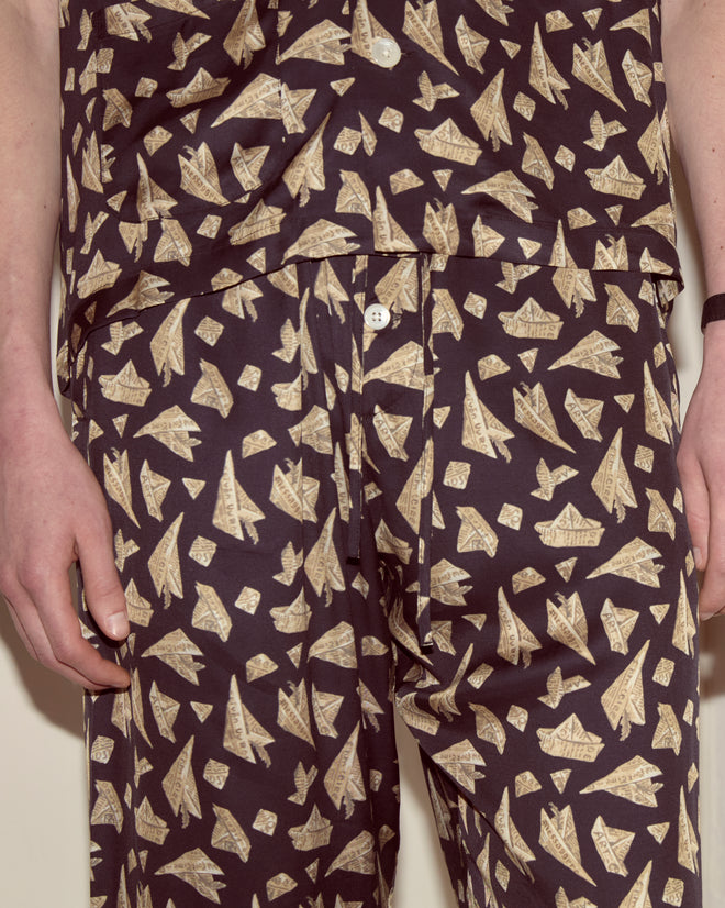 A person is shown from shoulders to thighs wearing matching dark clothes with a playful tan paper airplane print, featuring Paper Hat Pajama Pants with wide legs for a relaxed vibe.