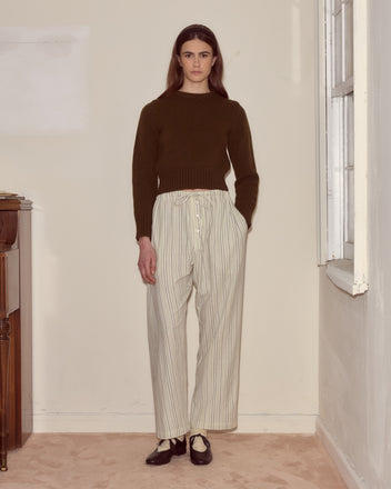 A person stands indoors by a window and piano, wearing a dark sweater paired with Electric Light Pajama Pants.