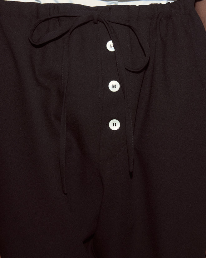Close-up of the Astor Pajama Pants in black, featuring a drawstring waist, four white front buttons, and made from heavyweight wool crepe for comfort and style.