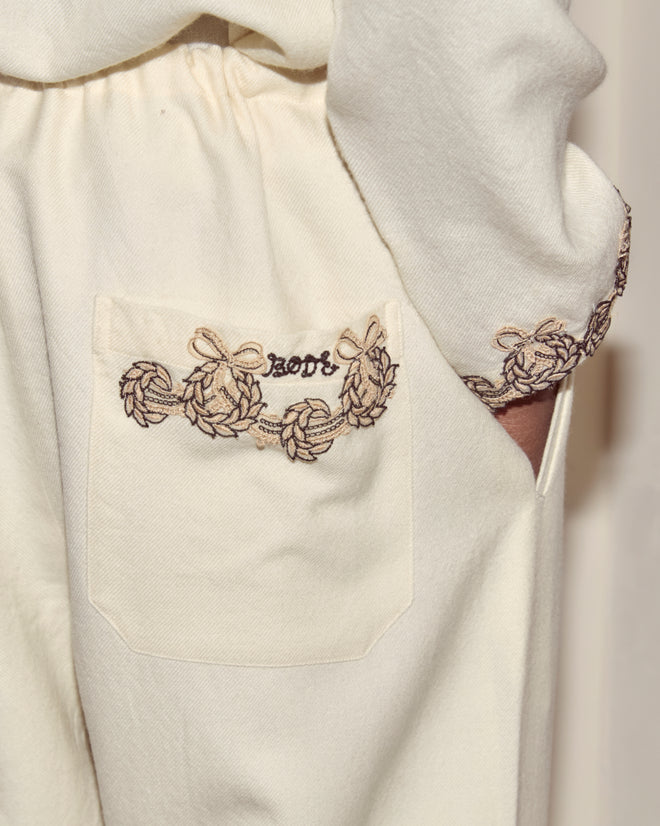 Close-up of Laurelist Pajama Pants - Cream in soft flannel, featuring an embroidered pocket, decorative brown stitching, and vintage passementerie accents.