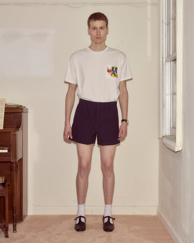 A man stands indoors wearing a white T-shirt, Field Shorts - Navy, white socks, and black shoes.