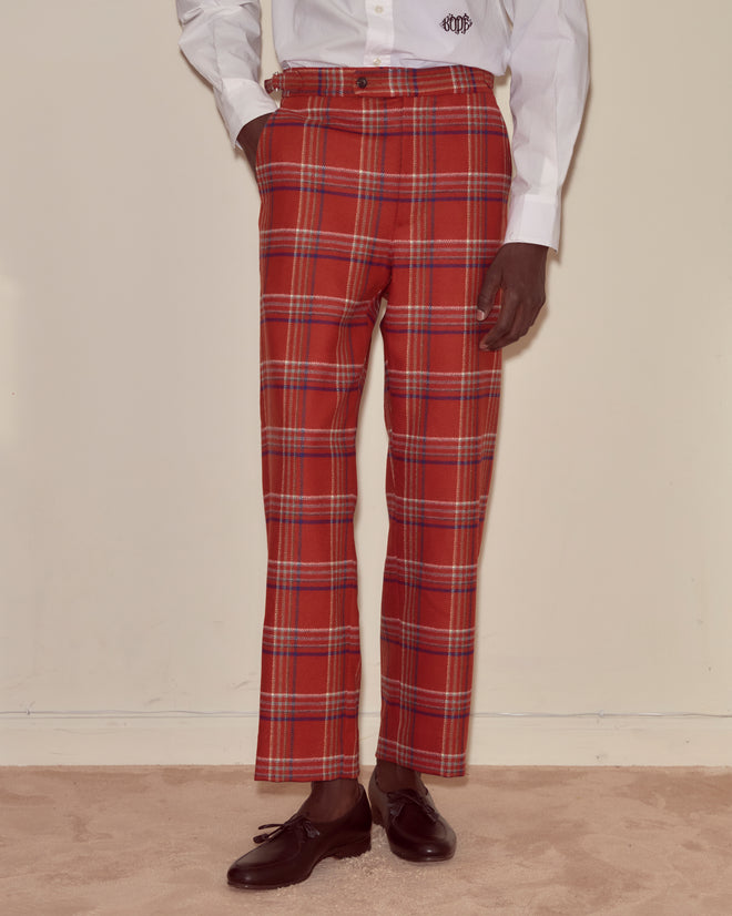 A person in Gable Plaid Trousers, a white shirt, and brown shoes stands on a beige carpet.