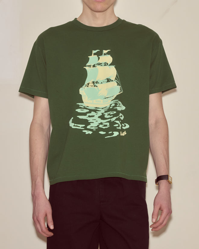 Someone wearing the Pirate Ship Tee, a 100% cotton green shirt with a sailing pirate ship and its reflection printed on the front.