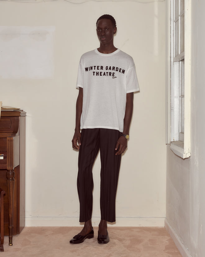 Indoors, someone wears the Theatre Tee—a white shirt inspired by Broadway favorites like Peter Pan—paired with black pants.