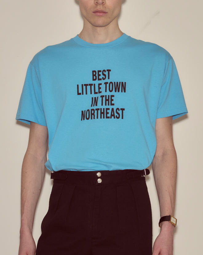 Person in a blue Laketown Tee with "BEST LITTLE TOWN IN THE NORTHEAST" text and high-waisted black pants—a classic Camp Onibar look inspired by the Poconos.