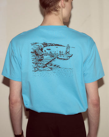 Person wearing a blue Laketown Tee featuring a black sketch of a lakeside scene with boats and people on the back, capturing the spirit of the Poconos.