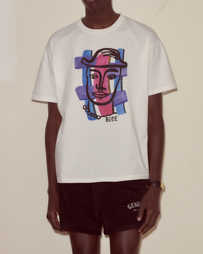 Person wearing the Chapeau Tee, a white graphic T-shirt with a modernist abstract face design, paired with black shorts.