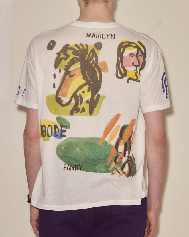 Person wearing the Collage Tee, a white souvenir shirt featuring colorful abstract colorblocking and the words "MARILYN," "BODE," and "SANDY" on the back.