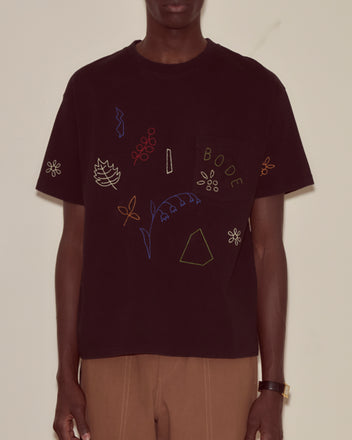 Wearing the Embroidered Field Guide Tee, made from black 100% cotton and featuring colorful embroidered leaves, flowers, and 