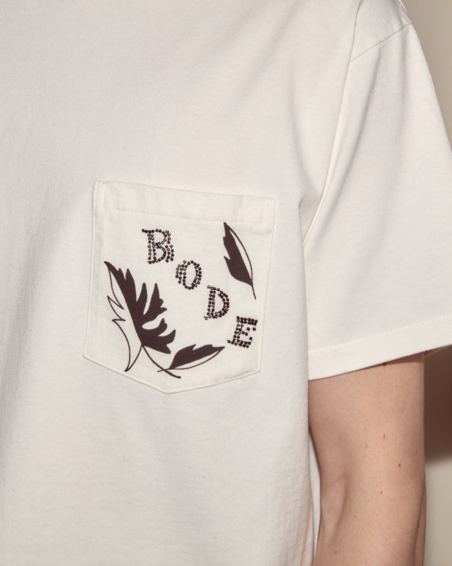 The Beaded Leaf Pocket Tee is a white 100% cotton Peter Pan tee featuring a chest pocket with black beaded leaf motifs and “BODE” spelled out in dotted letters.