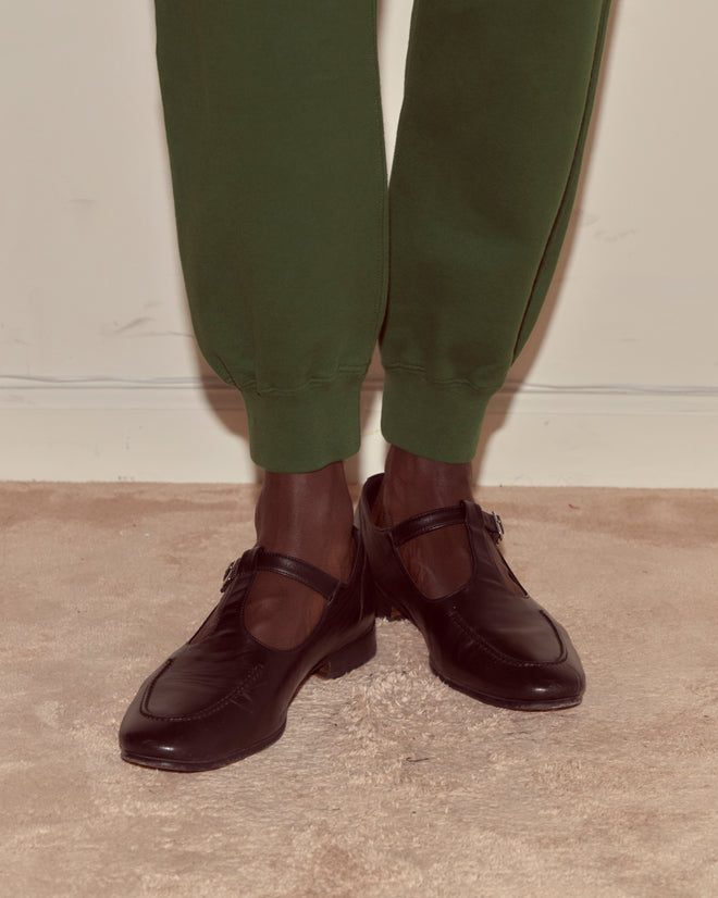 A person wearing Joggers - Dark Green with a Bode woven label and black dress shoes stands on a beige carpet.