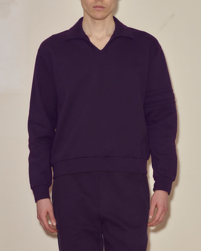 A person wearing a dark purple Crew Polo and matching pants stands against a plain background.