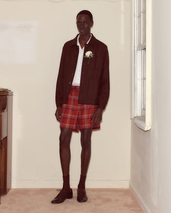 Wearing the Bramble Franck Jacket over a white shirt, red plaid shorts, and dress shoes, this person stands indoors by a window, mixing classic tailoring with playful 1960s-inspired workwear style.