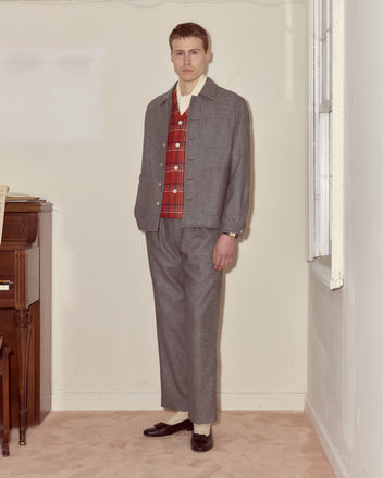 A man in a Dovecote Franck Jacket—heathered grey wool with novelty silver ship buttons and a red plaid vest—stands indoors by a piano, facing the camera.