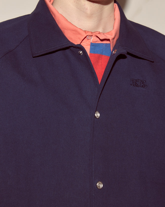 Person wearing a Twill Track Jacket - Navy over a coral collared shirt with a red and blue striped sweater underneath.